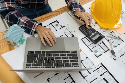 A close-up shot of an engineer in a checkered, long-sleeved polo shirt using a calculator to estimate a project’s value; only his hands are shown.