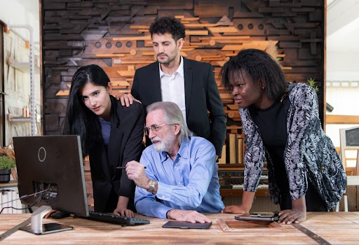 Two male and one female architect discuss plans for eco-friendly, cost-efficient buildings; a yellow hard hat rests on the blueprint.