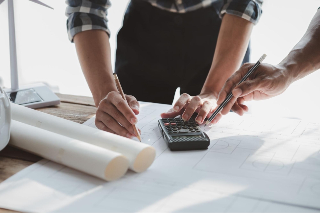 An architect and engineer are discussing the drafts with the help of blueprints and calculators to align with the budget