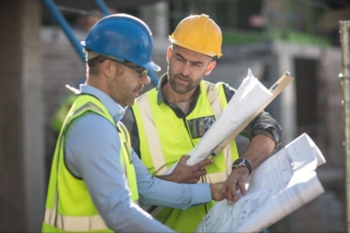 Two construction workers look over plans and blueprints.