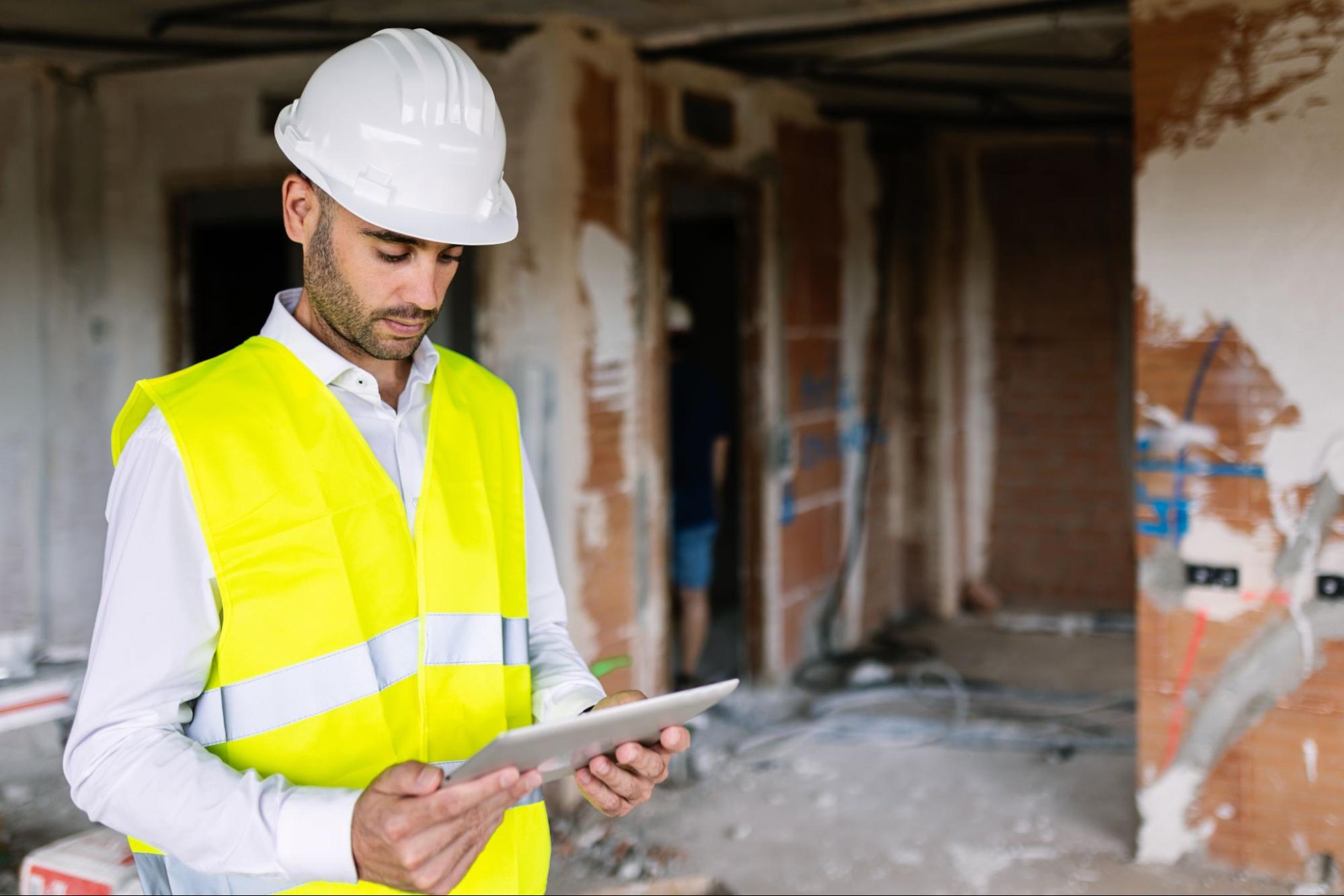 Young architect in safety gear using a digital tablet to assess a damaged building.