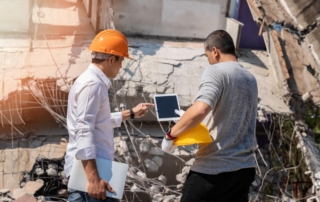 A male supervisor and foreman using a tablet to discuss restoration plans for a demolished building, highlighting the use of technology.