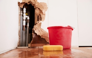 An image of a damaged exposing burst water pipes with a red bucket and sponge.