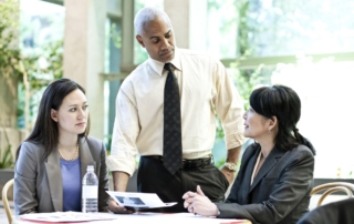 Three executives are in the meeting room discussing strategic business plans.