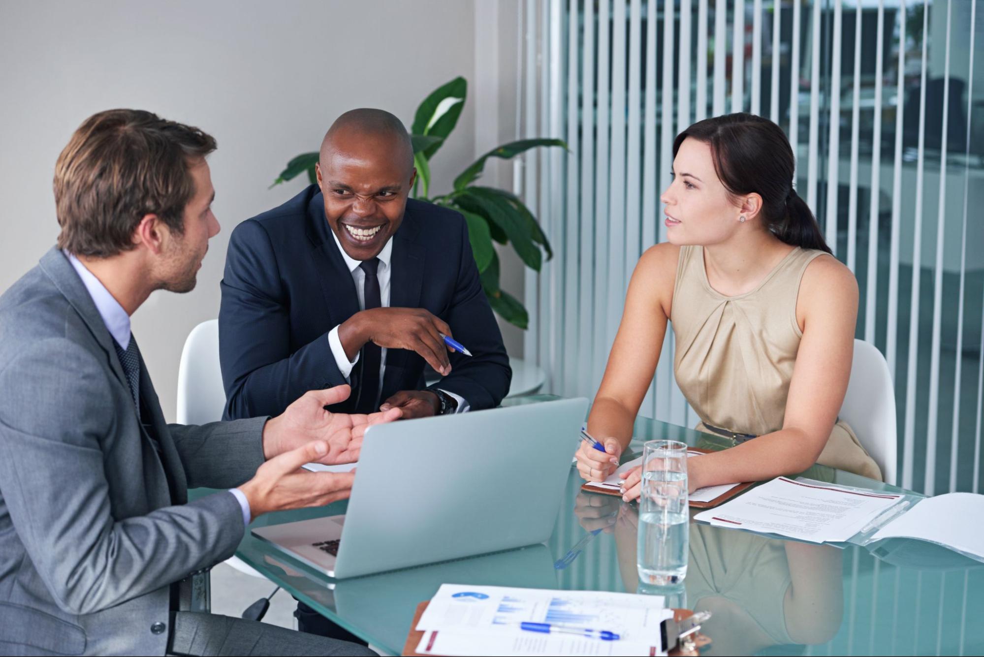 A business consultant presents strategies to two clients with a laptop, discussing growth opportunities and business improvements.