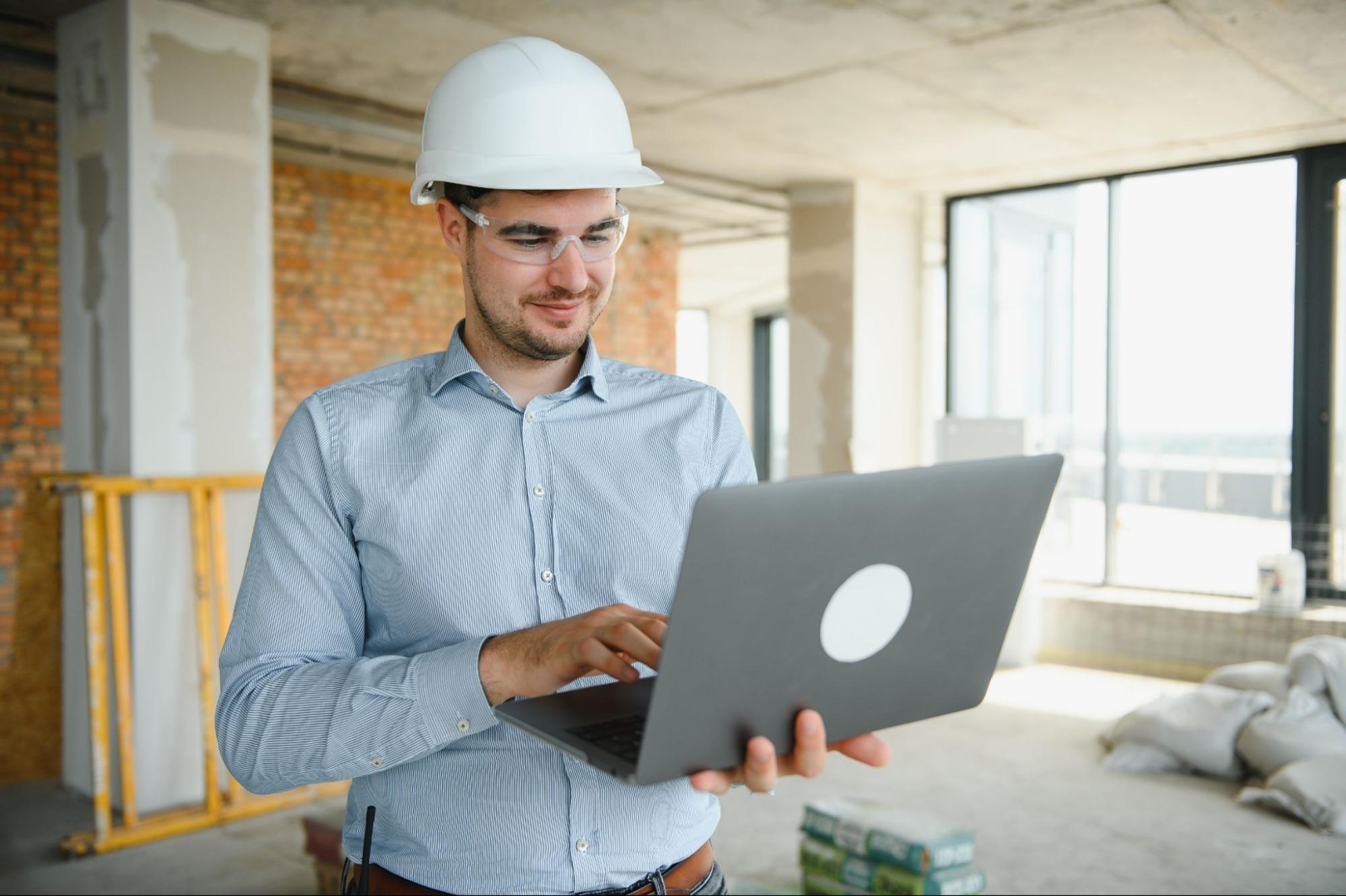 A male architect uses a construction site laptop to review project plans and estimates.