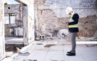 A man in safety gear assesses building damage, taking notes to provide accurate restoration cost estimates.