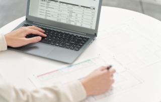 Using estimating software on a laptop, a man's hand cross-references details with notes on a sheet.