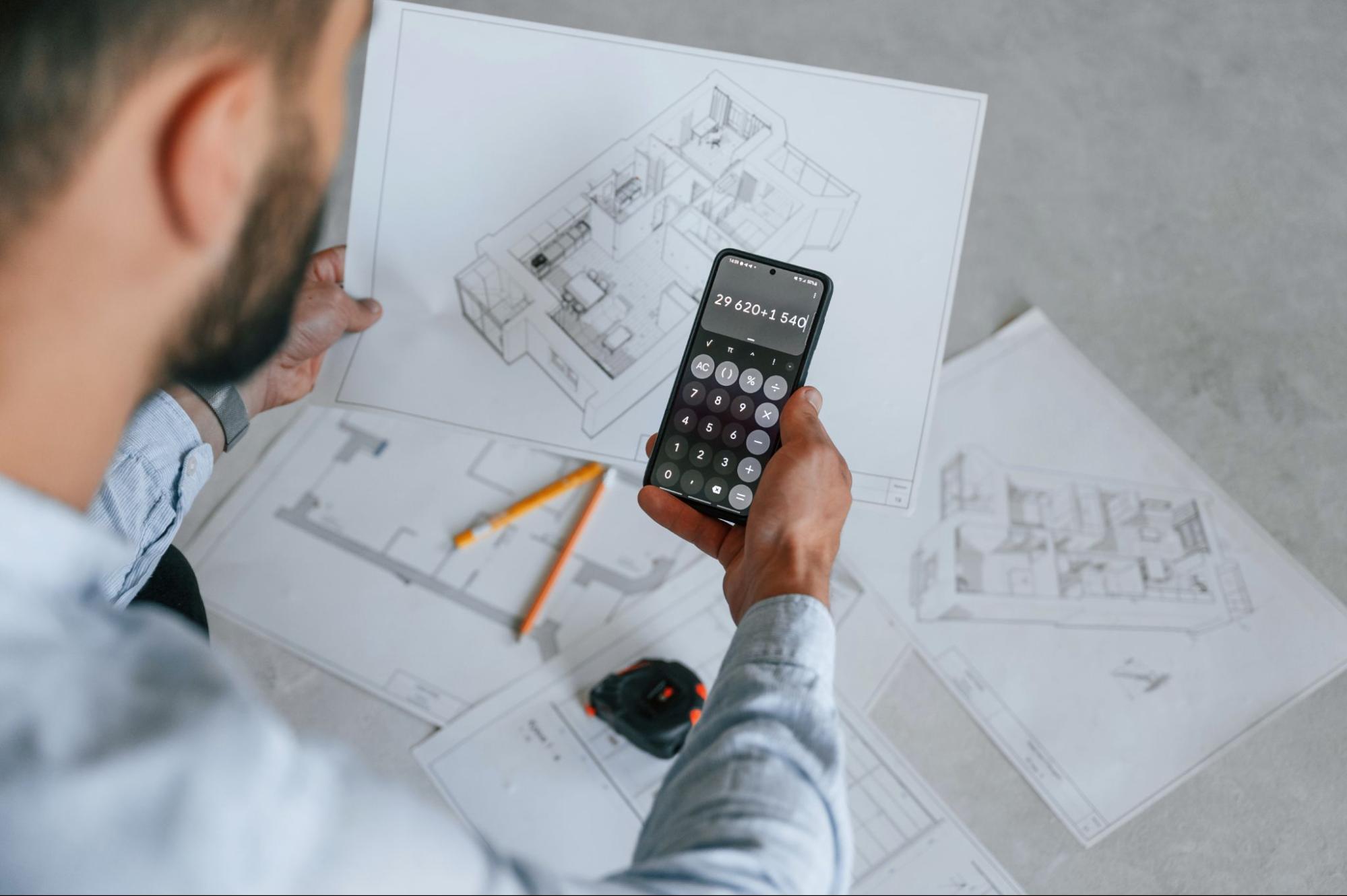 A man estimates the costs for his apartment renovation on his smartphone while looking at a blueprint.